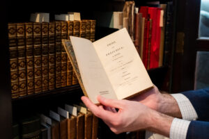 Hands hold open a small book revealing the text "Pride and Prejudice, a novel in three volumes"