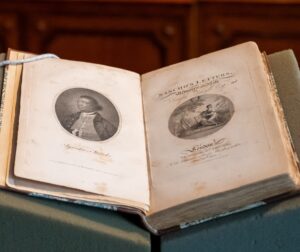 A small volume lies open on a desk revealing a sketch of Ignatius Sancho opposite text reading, "Letters of the Late Ignatius Sancho, An African, to which are Prefixed, Memoirs of his Life, by Joseph Jekyll"
