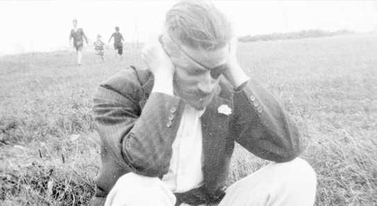A black and white photo of James Joyce crouched in a field with his head in his hands
